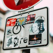 Straßenschild mit vielen Aufklebern, Fokus auf Free Assange Aufkleber